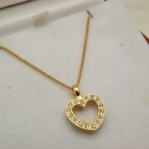 Un raffinato ciondolo di bigiotteria a forma di cuore e catena realizzati in metallo color oro e incastonati con scintillanti pietre bianche trasparenti sfaccettate e rotonde.