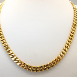 Un collar de bisutería con diseño de cadena larga plana y pesada, clásico y elaborado con eslabones planos de metal dorado pulido y un cierre con forma de langosta.