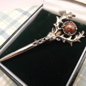 A lovely Scottish/Celtic Jacobite sword and stags head brooch/kilt pin made in silvertone metal set with a brown mottled stone in the center