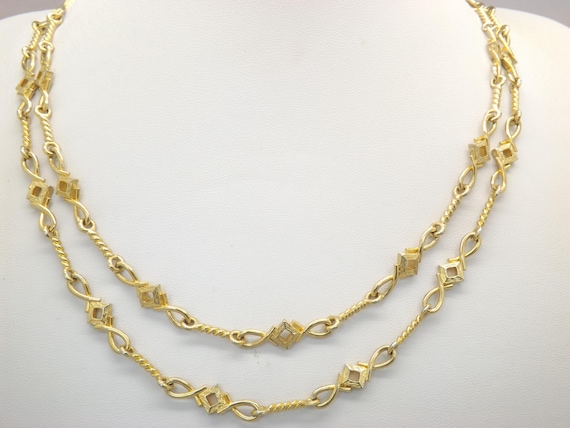 A fancy long goldtone chain costume jewelry necklace set along its length with mixed patterns and shapes in goldtone metal.