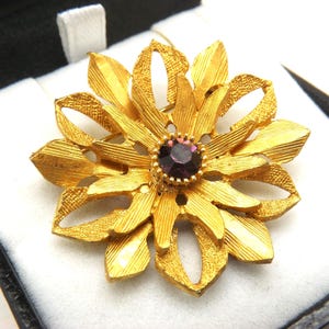 A superb round flower head shape costume jewelry period brooch in openwork goldtone metal set in the center with a purple stone
