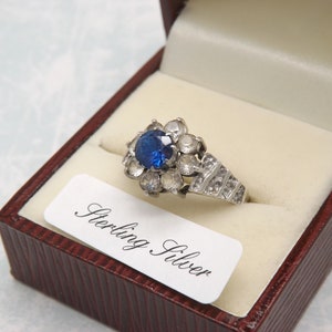 A fine 9ct gold and silver vintage jewelry dress ring set with a sapphire blue center stone surrounded by clear CZ diamond type hard stones
