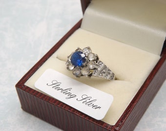 A fine 9ct gold and silver vintage jewelry dress ring set with a sapphire blue center stone surrounded by clear CZ diamond type hard stones