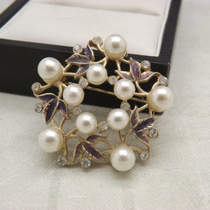 A lovely round flower spray design vintage jewelry brooch made in goldtone metal and enamel with faux pearls and clear white sparkly stones