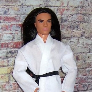 May include: A white karate uniform with a black belt. The uniform has long sleeves and pants. The model has long black hair and is wearing a white karate uniform with a black belt.