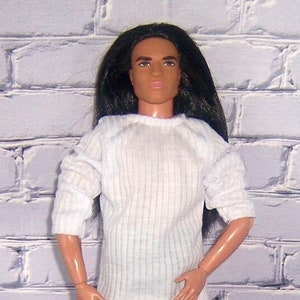 May include: A doll wearing a white ribbed sweater and blue jeans. The doll has long black hair and brown eyes.