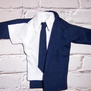 May include: A white dress shirt with a dark blue tie and a dark blue blazer. The blazer is unbuttoned and the shirt is visible underneath.