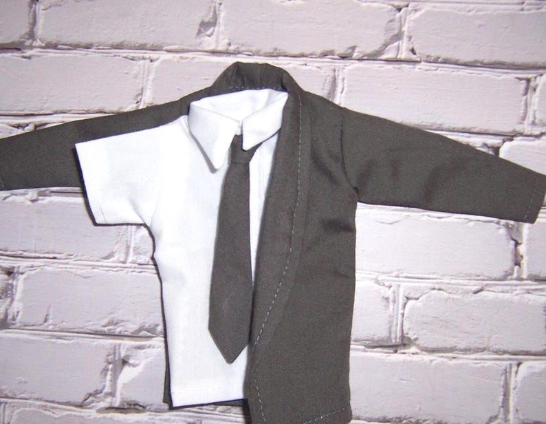 K&ouml;nnte beinhalten: Eine dunkelgraue Jacke mit langen &Auml;rmeln &uuml;ber einem wei&szlig;en kurz&auml;rmeligen Hemd mit Kragen. Eine passende dunkelgraue Krawatte ist mittig &uuml;ber dem wei&szlig;en Hemd platziert. Das Kleidungsst&uuml;ck weist sichtbare N&auml;hte entlang des Revers auf.