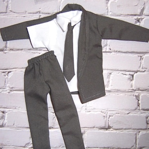 K&ouml;nnte beinhalten: Ein dunkelgrauer Anzug mit lang&auml;rmeliger Jacke, wei&szlig;em Hemd mit Kragen, dunkelgrauer Krawatte und passender Hose mit elastischem Bund. Das Set ist als Miniatur-Outfit f&uuml;r eine Puppe oder eine kleine Figur konzipiert.