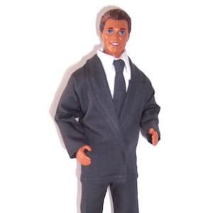 K&ouml;nnte beinhalten: Eine Kunststoffpuppe mit braunen Haaren und blauen Augen, bekleidet mit einem dunkelgrauen Sakko, einer passenden Hose, einem wei&szlig;en Hemd mit Kragen und einer dunkelgrauen Krawatte. Die Puppe hat einen neutralen Gesichtsausdruck und steht aufrecht.
