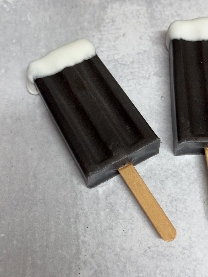 May include: Two chocolate popsicles with white chocolate topping on a stick. The popsicles are on a gray surface.