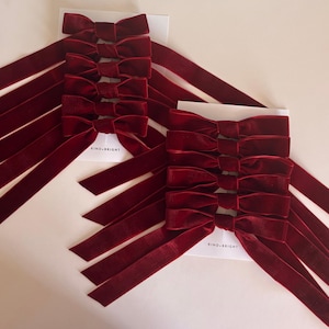 May include: Burgundy velvet bows with long tails, arranged on white cards. Each card has the text "KIND.BRIGHT" printed on it. The bows are neatly stacked, showcasing their rich color and texture, perfect for crafting or gift wrapping.