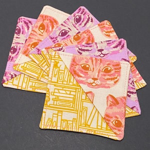 May include: Set of six pink and orange cat-themed fabric coasters with a bookshelf pattern on the back. The coasters are made of cotton fabric and have a pink and white background with a yellow bookshelf pattern.
