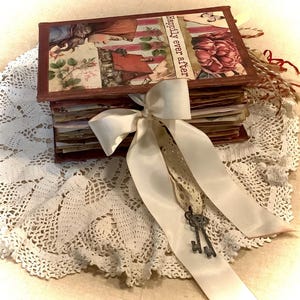 May include: A decorative wooden box with a collage-style design featuring floral and vintage imagery. The box is tied with a cream-colored satin ribbon and a vintage key charm. The text "Happily ever after" is visible on the box.