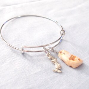 May include: A silver bangle bracelet with a mermaid charm and a natural shell charm.