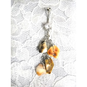 May include: A silver body jewelry piece with a clear crystal charm and three dangling seashells in shades of brown and orange.