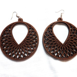 May include: A pair of large, round, brown wooden earrings with a delicate, intricate laser-cut design. The earrings have a teardrop-shaped cutout in the center.