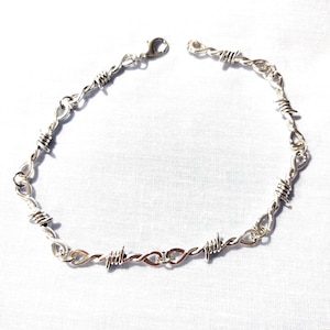 May include: A silver chain necklace with a barbed wire design. The necklace is made of metal and has a clasp closure.