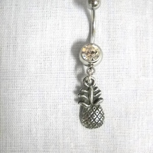 May include: A silver belly button ring with a clear crystal and a pineapple charm.