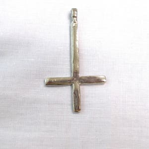 May include: A silver upside-down cross pendant. The cross is made of metal and has a hammered texture.