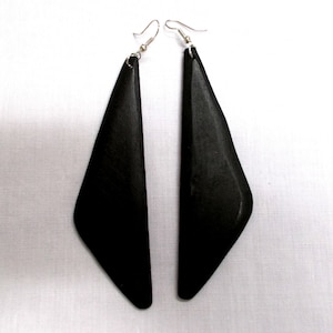 May include: A pair of long, black, wooden earrings with a triangular shape. The earrings have silver hooks.