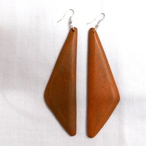 May include: A pair of long, brown wooden earrings with a triangular shape. The earrings have a silver hook.