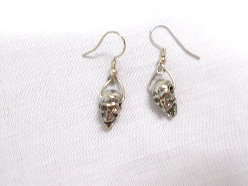 May include: A pair of silver skull dangle earrings. The earrings have a simple hook design and feature a small, detailed skull charm.