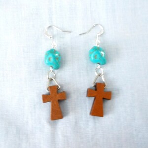 May include: A pair of dangle earrings with turquoise skull beads and brown wooden cross charms.