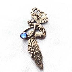 May include: Silver pendant featuring a detailed fairy figure with wings and a blue gemstone. The fairy is holding a sphere in her hand.