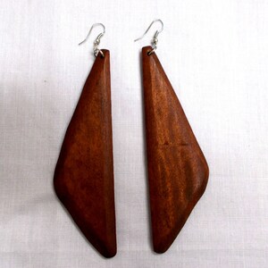May include: A pair of wooden earrings with a triangular shape. The earrings are a rich, dark brown color and have a smooth, polished finish. The earrings hang from silver-colored hooks.