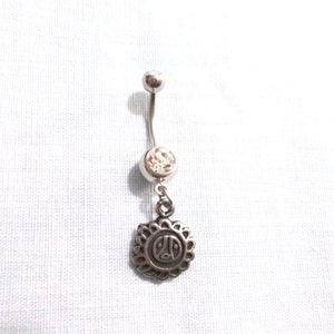 May include: Silver belly button ring with a clear crystal and a dangling charm featuring a peace sign inside a circle.