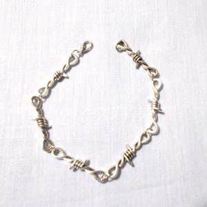 May include: A silver barbed wire necklace with a clasp closure.