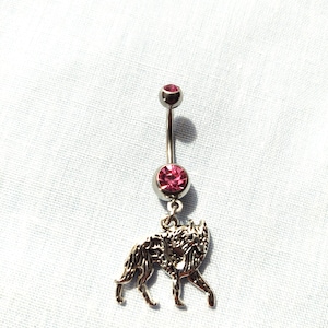 May include: A silver belly button ring with a pink gem and a wolf charm.