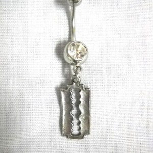 May include: A silver body piercing with a clear crystal and a razor blade charm.