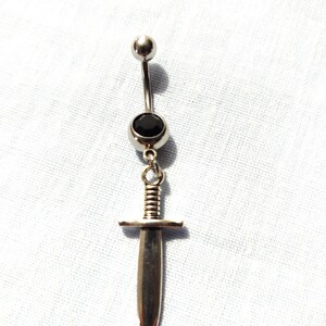 May include: Silver body piercing with a black gem and a dangling sword charm.