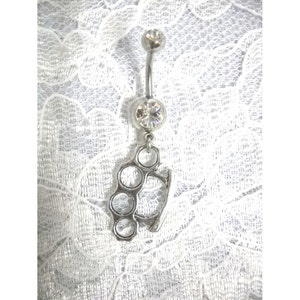 May include: Silver belly button ring with a clear crystal and a dangling silver charm shaped like a brass knuckle.