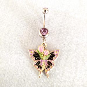 May include: A silver body jewelry piece with a butterfly charm. The butterfly is black with pink and green accents and has a bouquet of pink tulips in the center. The jewelry has two pink gem stones.