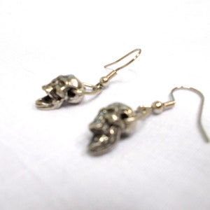 May include: A pair of silver skull dangle earrings. The skulls are detailed and have an open mouth.