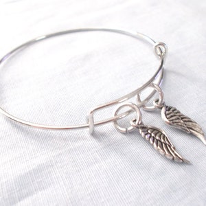 May include: A silver bangle bracelet with two dangling silver charms shaped like wings.