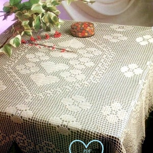 Pode incluir: Uma toalha de mesa de crochê branca com um delicado padrão floral. A toalha de mesa está colocada sobre uma mesa com uma pequena caixa com padrão floral no topo. O texto "PDF Mary Pattern" é visível em um coração azul.
