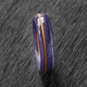 May include: A purple and brown wooden ring with a light brown inlay. The ring is made of wood and has a smooth finish.