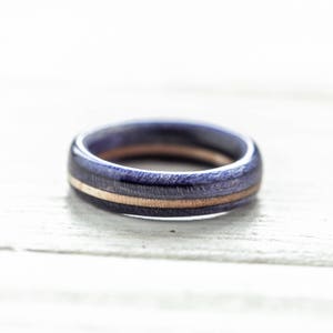 May include: A wooden ring with a purple and brown striped pattern. The ring is made of wood and has a smooth finish.