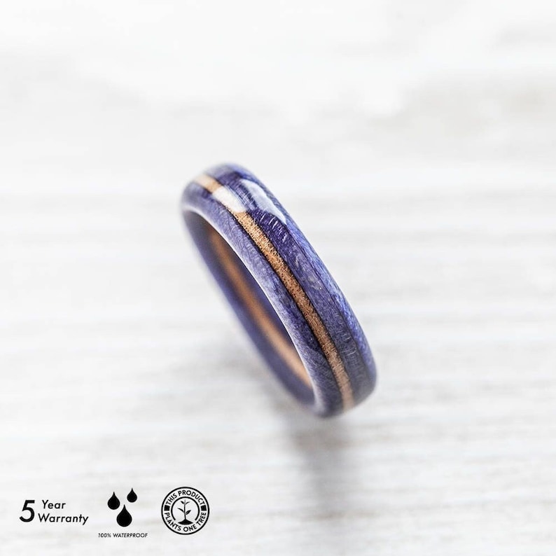 May include: A close-up of a purple and brown wooden ring with a white stripe. The ring is made of wood and has a smooth finish. The ring is waterproof and comes with a 5-year warranty. This product plants one tree for every purchase.