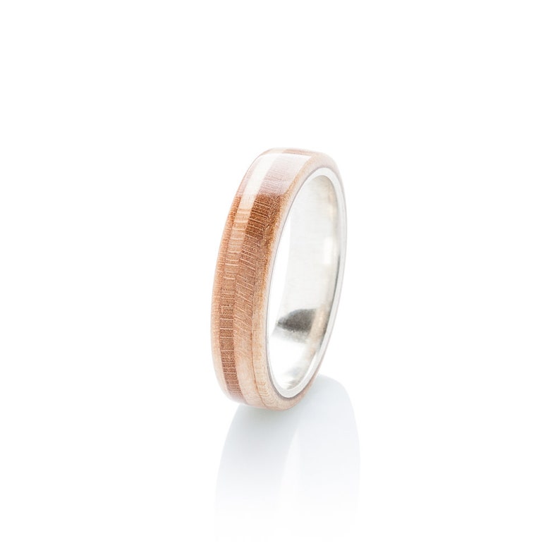 May include: A wooden ring with a silver band. The wood is a light brown colour with darker brown stripes.