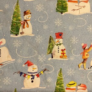 Snowman Fabric features different snowmen scenes and a little boy building a snowman on a blue background. 100% cotton by The Craft Cotton Company.