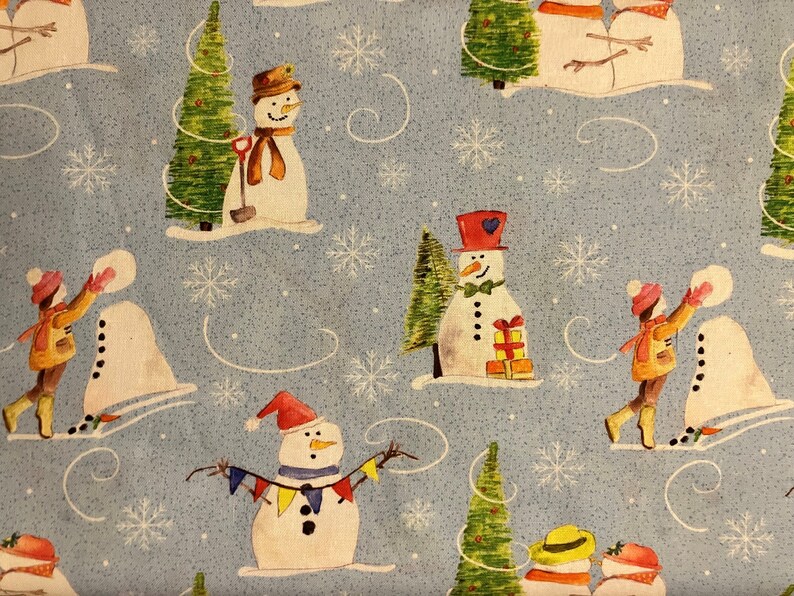 Snowman Fabric features different snowmen scenes and a little boy building a snowman on a blue background. 100% cotton by The Craft Cotton Company.