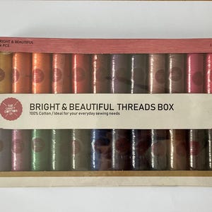 May include: A box set of 24 spools of sewing thread in a range of colours. The box is labelled "BRIGHT & BEAUTIFUL THREADS BOX" and includes shades of orange, pink, green, and blue. The threads are made from 100% cotton.