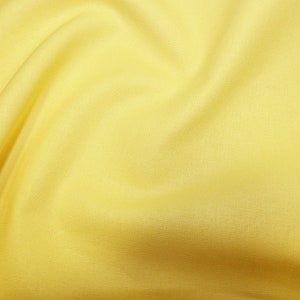 May include: A smooth, yellow fabric with a soft, flowing texture. The fabric is draped and folded, creating a subtle pattern of light and shadow.