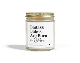 May include: A white candle jar with a gold lid. The label reads "Badass Babes Are Born in October" with a small heart symbol. The candle is infused with confidence and style.