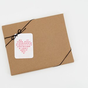 May include: A brown paper gift bag with a black string tied around it. A white tag with a pink heart made of smaller hearts is attached to the string.